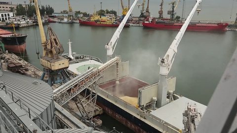 Timelapse of ship loading grain crops on bulk freighter via trunk to open cargo holds at silo terminal in seaport. Cereals bulk transshipment to vessel. Transportation of agricultural products.