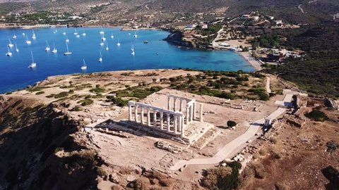 Aerial drone bird's eye view video of boats docked near iconic archaeological site of Cape Sounio, Ancient temple of Poseidon, Attica, Greece