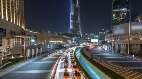 Car traffic on road near mall at night in downtown timelapse hyperlapse. Skyscrapers with night illumination. Top view from bridge. Dubai, UAE
