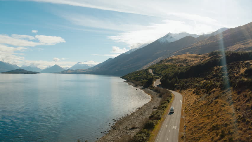 Rising drone shot of van driving beside blue lake in New Zealand Royalty-Free Stock Footage #1011917354