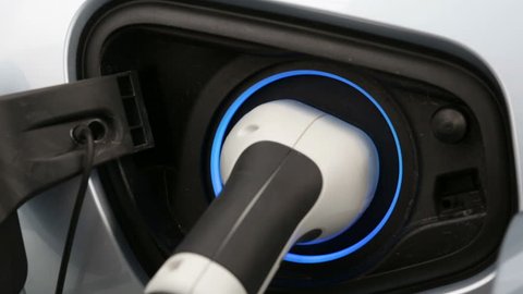 Electric car charger plugged in an electric vehicle. Zoom out.