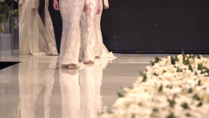 Female models walk the runway in different white dresses during a Fashion Show. Fashion catwalk event showing new collection of clothes. In a row.4k. Royalty-Free Stock Footage #1011921782