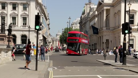 London, England - May 2018: Buses turn from Pall Mall while people wait at a pedestrian crossing. The dome of the National Gallery is clearly visible at the end of Pall Mall