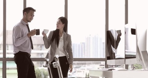 Businessman and businesswoman standing and drinking coffee while talking in modern office