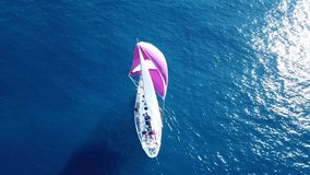 Aerial drone bird's eye view video of beautiful purple sail boat cruising in deep blue ocean