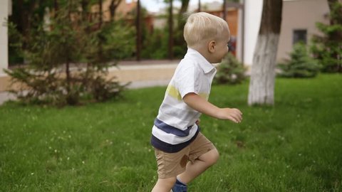 A little boy is playing with his father in hide and seek in the garden. He is happily running on the grass. The father catches his son, raises to his hands and turns him around. Slow motion