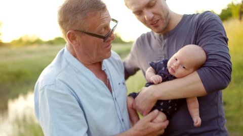 Three generations of one family embrace. Men rest on the river bank. Grandpa, son and grandson spend time together. Happy family vacation
