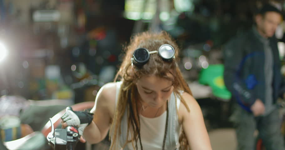 A stylish female biker makes maintenance of her motorcycle in the garage. in slow motion