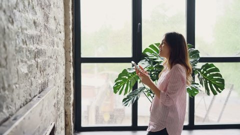 Pretty brunette house owner is decorating her loft style room hanging picture on brick wall choosing place. Interior design, housework, decorating apartment and people concept.