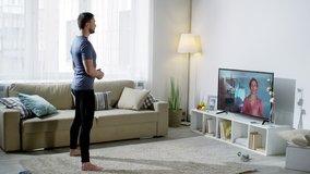 Wide shot of man in sportswear looking at online personal trainer on TV screen and doing boxer squat punch exercise at home