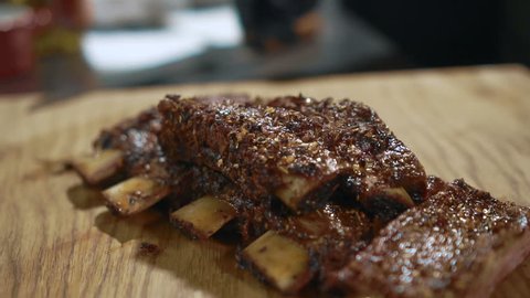 Close up of grilled beef ribs are being served at the kitchen of restaurant, slow motion.