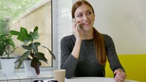 Young beautiful woman with ponytail sitting in cafe, talking on phone and smiling, happy