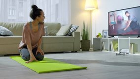 PAN of young woman doing plank on yoga mat while training at home with online personal coach