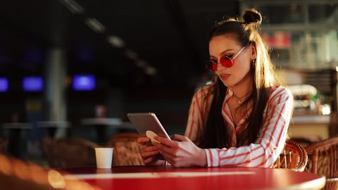 Young attractive woman in red sunglasses with tablet computer sitting in cafe. Beautiful girl in airport or shoppping mall with tablet