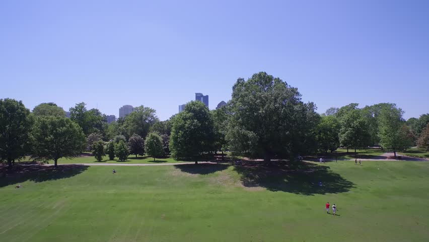 Slow zoom in to the Atlanta skyline, flying over a park with a lake 
