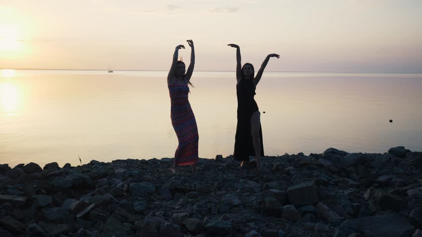 Carefree women in long black dress dancing on beach at sunset.