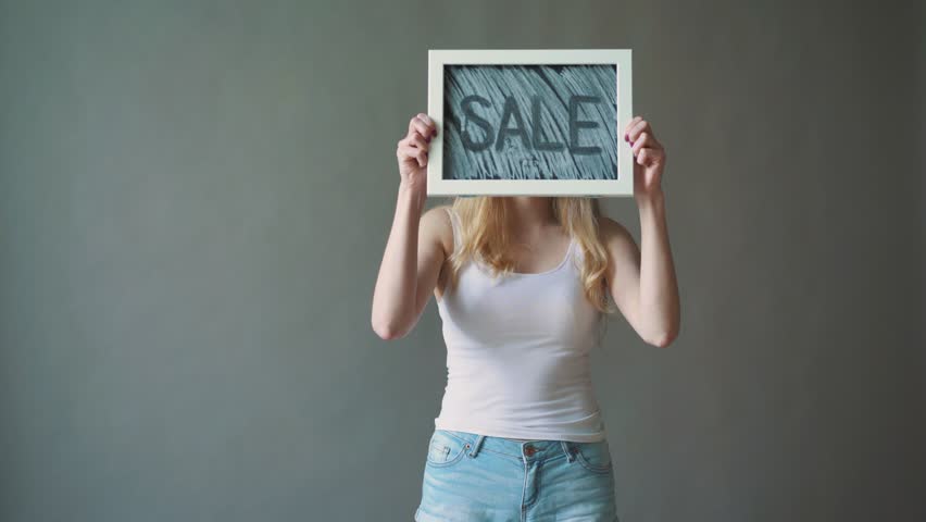 the girl shows a sign "SALE". gray background.