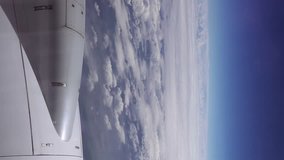 Flying over the clouds. View from plane aircraft passenger window. Clouds and skyline horizon panoramic view. Vertical format video.