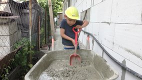 Little boy builder shakes with concrete shovel