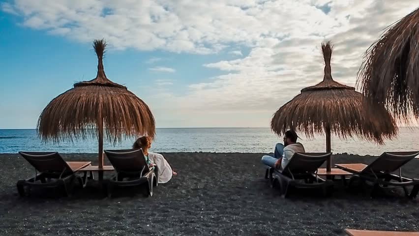 nice couple in love seats and lay down at the beach on the seats under the umbrellas to protect from the sun. tenerife summer vacation time leisure to anjoy the season and the sunset that come
 Royalty-Free Stock Footage #1011971390