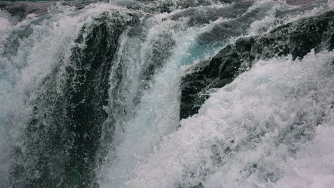 Powerful raging waterfall falling forcefully over a rocky edge. Crystal clear glacier water stream dropping over the cliff. Slow Motion Close up.