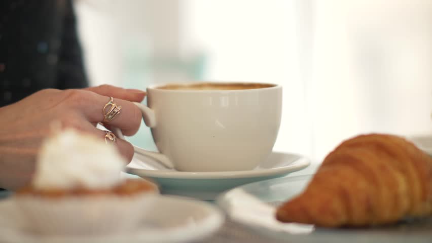 Woman drinking coffee from white cup at table in bakery cafe close up | Shutterstock HD Video #1011983354