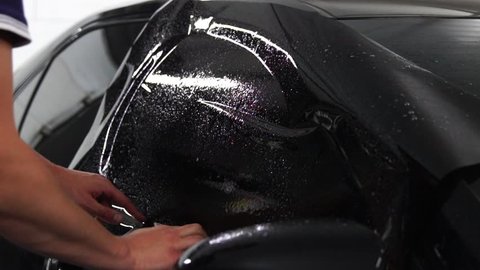 Master installs tint film for car glass with hairdryer and spatula with glare of light. Concept tinting