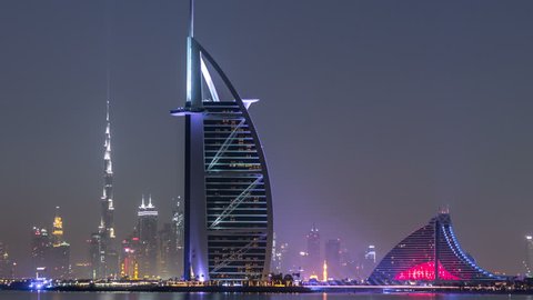 Skyline of Dubai by night with Burj Al Arab from the Palm Jumeirah timelapse. Illuminated skyscrapers reflected in water