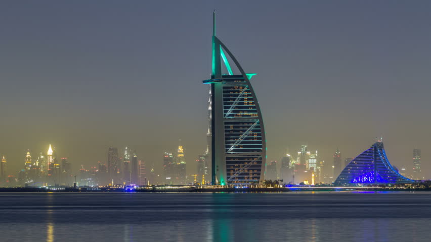 Skyline of Dubai by night with Burj Al Arab from the Palm Jumeirah timelapse hyperlapse. Illuminated skyscrapers reflected in water