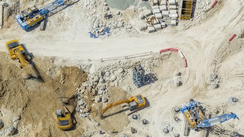 Large construction site including several excavators and cranes timelapse working on a building complex. Aerial top view from above at sunny day in Dubai, UAE