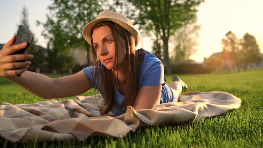 Girl making a selfie lying down on a blanket in the park at sunset
