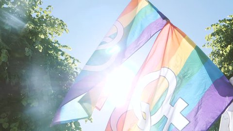 Sunlight flare over lesbian and gay gender symbols on two gay rainbow flag in slow motion at Lesbian Gay Bisexual Transgender LGBT GLBT visibility march pride - waving in slow motion