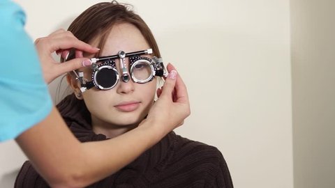 Young woman is on a doctor appointment in ophthalmological clinic. Optician is regulating optical trial frame, close-up of face