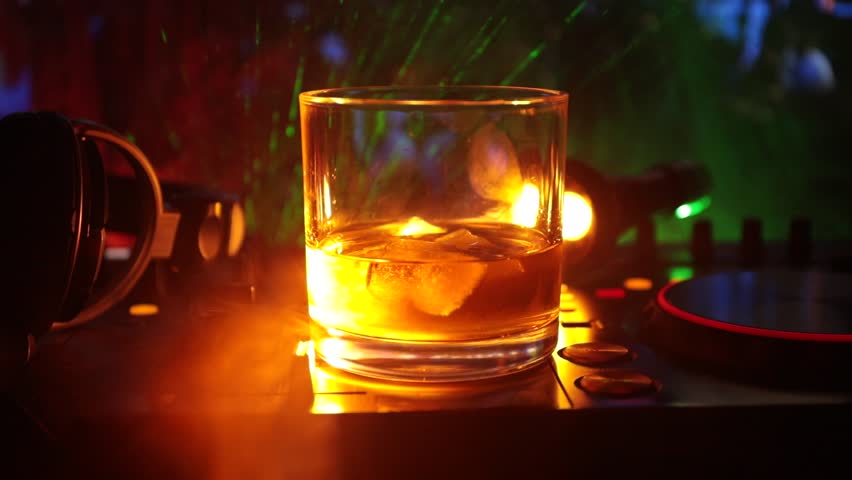 Glass with whisky with ice cube inside on dj controller at nightclub. Dj Console with club drink at music party in nightclub with disco lights. Slider shot | Shutterstock HD Video #1012001123
