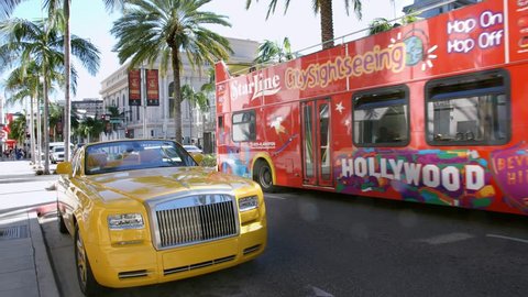 LOS ANGELES, CALIFORNIA, USA - JANUARY 8, 2015: Sightseeing tourist bus passing luxury Rolls-Royce luxury car and fashion boutique stores on Rodeo Drive in Beverly Hills, Los Angeles, California, 4K