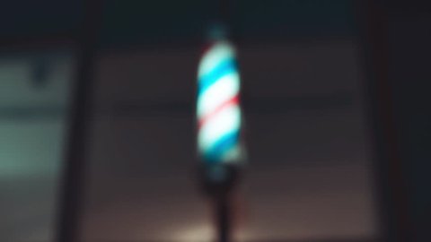 Barber pole spinning at night. International barbershop pole sign. Video with shaking. Soft focus.