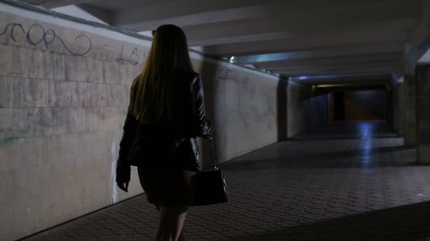 Back view of woman walking alone in subway passage at night. Man in hoodie steals bag from female's hand. Frustrated girl trying to chase robber. Upset woman gesturing with frustration. Steadicam