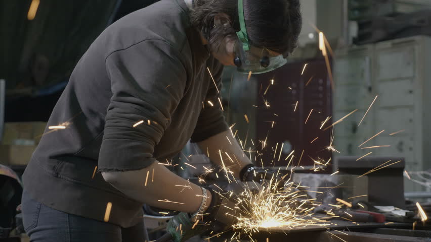 Professional woman welder or blacksmith employee wearing protection equipment grinding smooths steel and iron in an industrial workshop | Shutterstock HD Video #1012016444