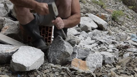 Young adult man (artisan/artist) who splits the rock with a hammer and chisel outdoors