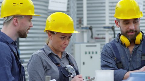 Tracking shot of three people in hard hats standing by fertigation machine, man talking to colleagues and explaining how to use new equipment