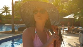 Beautiful girl in blue hat strolls by pool. Summer sun. Slow motion