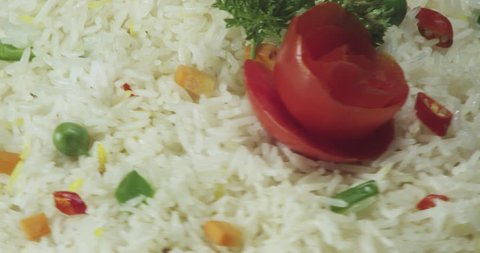 Cooked white rice or Vegetable biryani garnished with peas, green beans, carrots , parsley , and rose shaped cut tomatoes. See this plate rotate and create various perspectives of stylised food. 4k