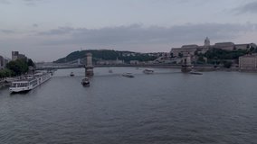 Dense traffic on and cruise ships below the Chainbridge crossing the Danube river in central Budapest - aerial video taken by a drone
