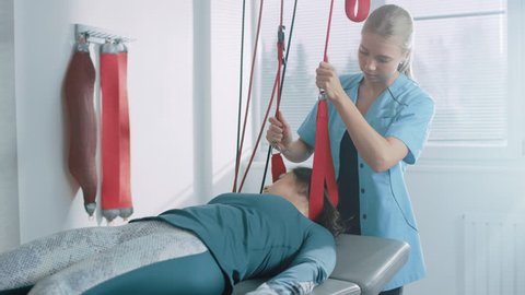 Physiotherapist Assists Female Patient with Trauma, Undergoing Rehabilitative Physiotherapy on a Special Suspension Rope System. Relieving Neck, Back, Head Pain. Shot on RED EPIC-W 8K Camera.