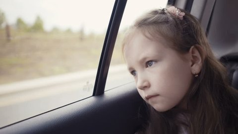 Little girl looking out from car window at sunny day