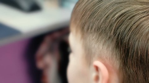 Barber cutting boy's hair with clipper. Back view of unrecognizable boy.