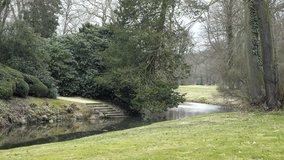Castle park with stream. Ornamental garden with small river. Spring melancholic landscape. Swim pond with plants, swimming area