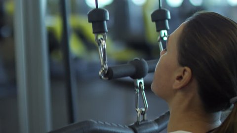 Slowmo of woman doing front pull-down exercise on machine in gym