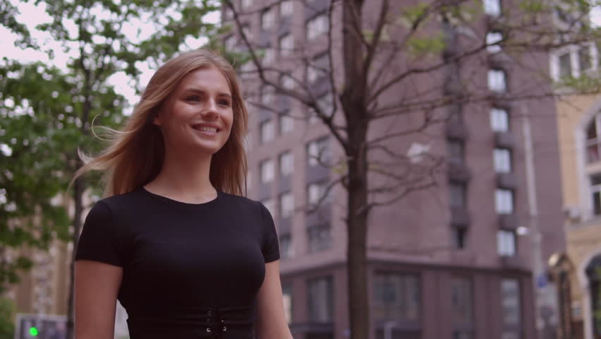 smiling woman walks outdoor slow motion. attractive blonde wearing elegant black dress. happy young girl walks in city