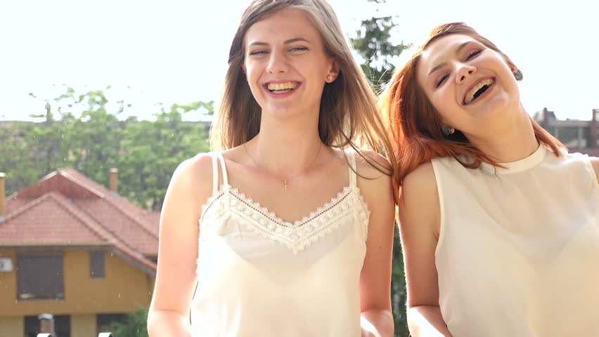 Two women on the balcony laughing and smiling while it is raining outside and the wind it is blowing through there hair. Super slow motion at 180fps